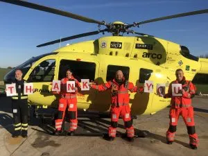Photo of Yorkshire Air Ambulance crew in front of helicopter holding up letters that spell out Thank You