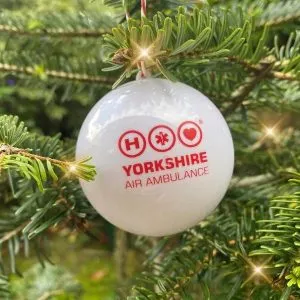 White ball with red Yorkshire Air Ambulance logo on, hung on a Christmas tree
