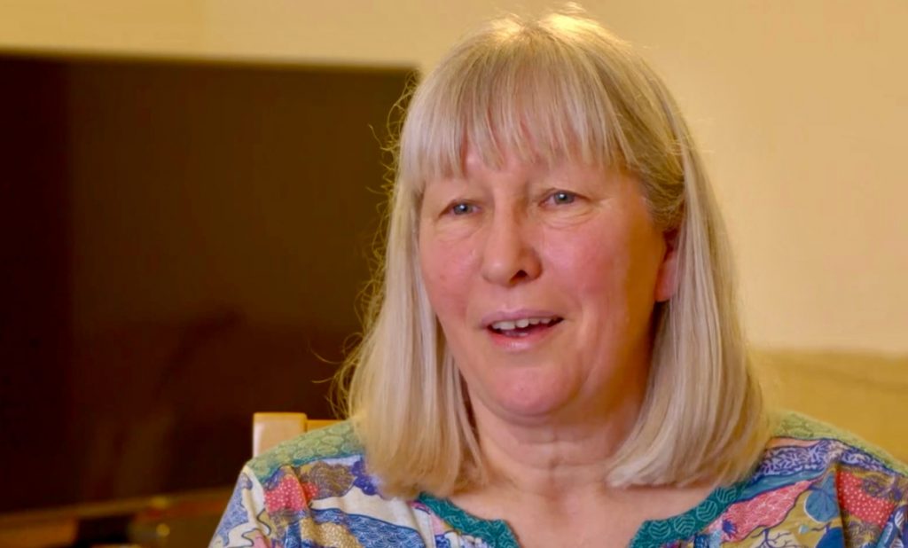 Photo of the head and shoulders of a lady, Stella Collins, who has shoulder length blonde hair and is wearing a multi coloured top.