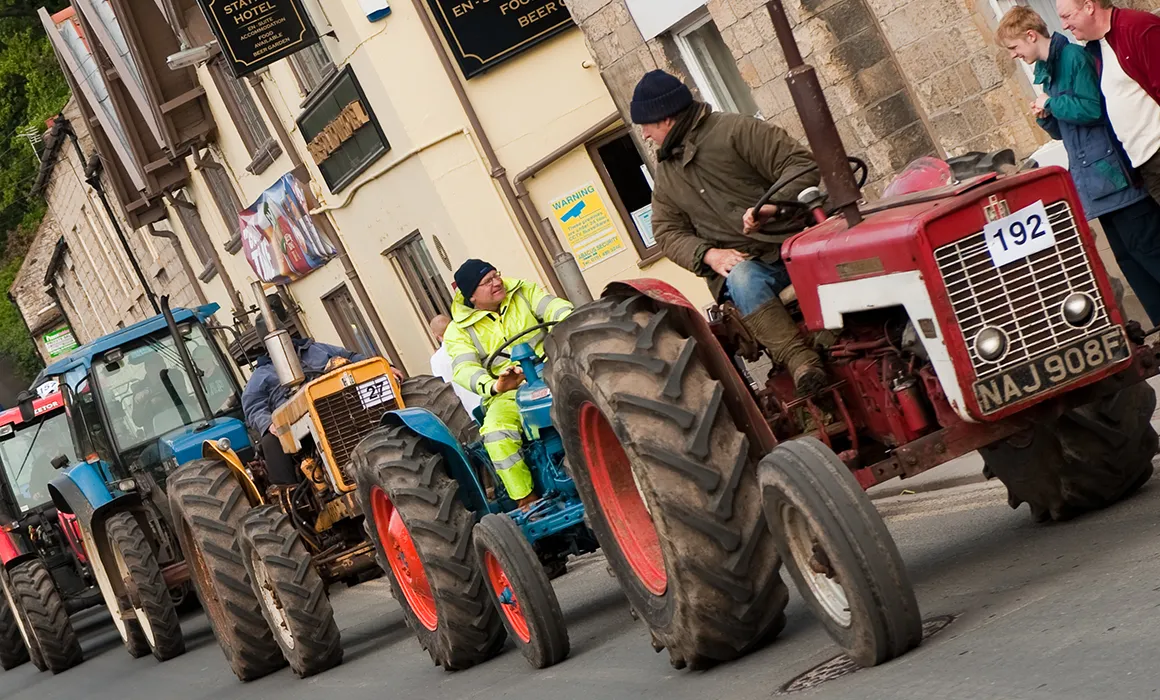 A number of tractors passing through a village.