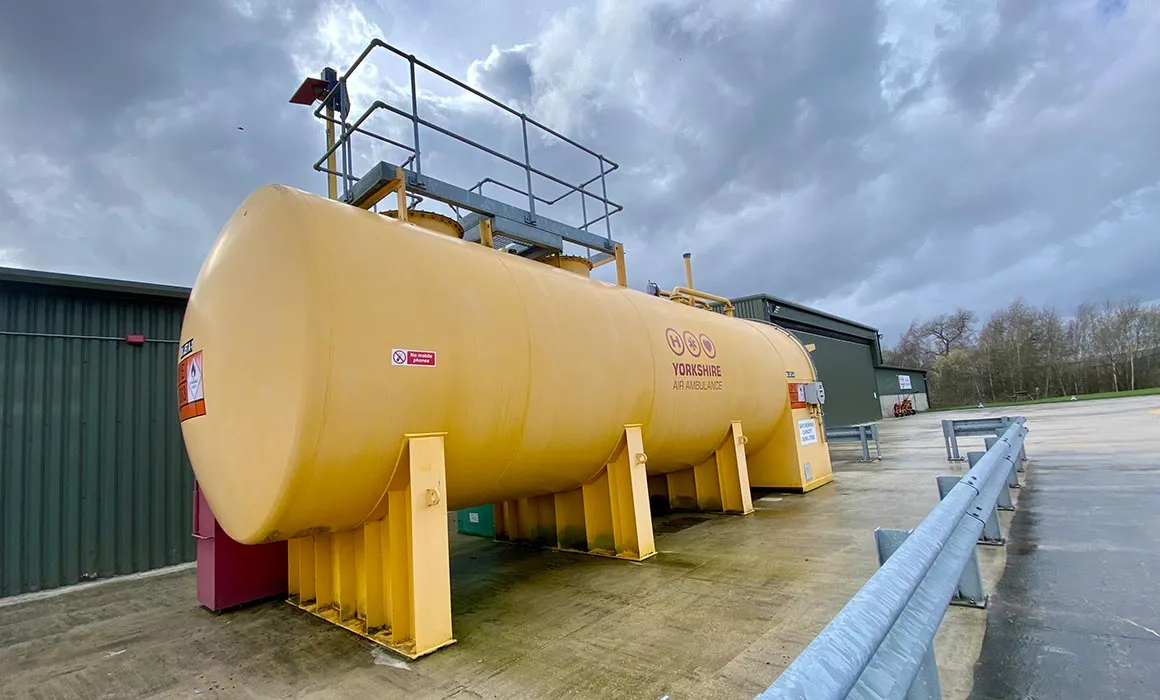 A larger yellow fuel container in front a green building. There is a red Yorkshire Air Ambulance logo on the fuel bowser.