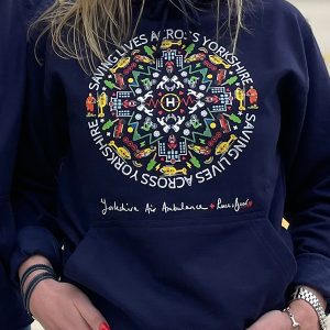 A close up of a person wearing a blue jumper or hoodie. There is a circular graphic on the front and some wording.