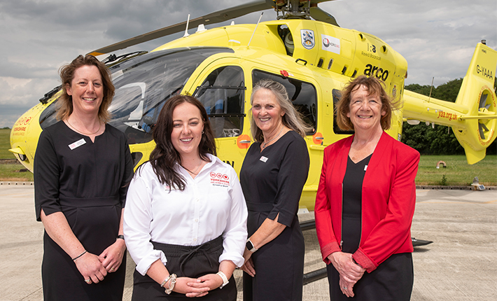 Four women are stood in front of a yellow helicopter