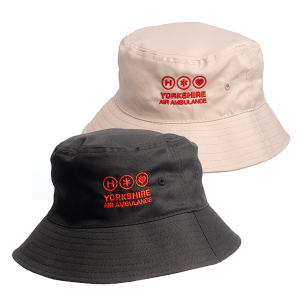 A black bucket had with red embroidered logo featuring the words 'YORKSHIRE AIR AMBULANCE', in front of a sand coloured bucket hat which features the same logo.