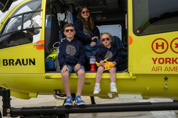 Three children wearing L&B YAA hoodies, sitting in a YAA Helicopter