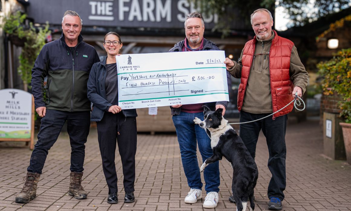 Four people and a dog stood in front of a Farm Shop sign holding a big cheque.