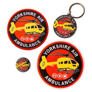 A round fabric patch, metal keyring, metal badge and sticker, all featuring a yellow helicopter and the words YORKSHIRE AIR AMBULANCE. The items are on a white background.