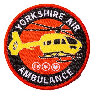 A round fabric patch featuring a yellow aircraft on a red background with the words YORKSHIRE AIR AMBULANCE