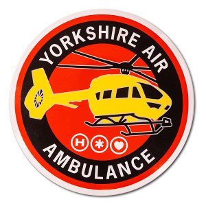 A round sticker featuring a yellow aircraft on a red background with the words YORKSHIRE AIR AMBULANCE