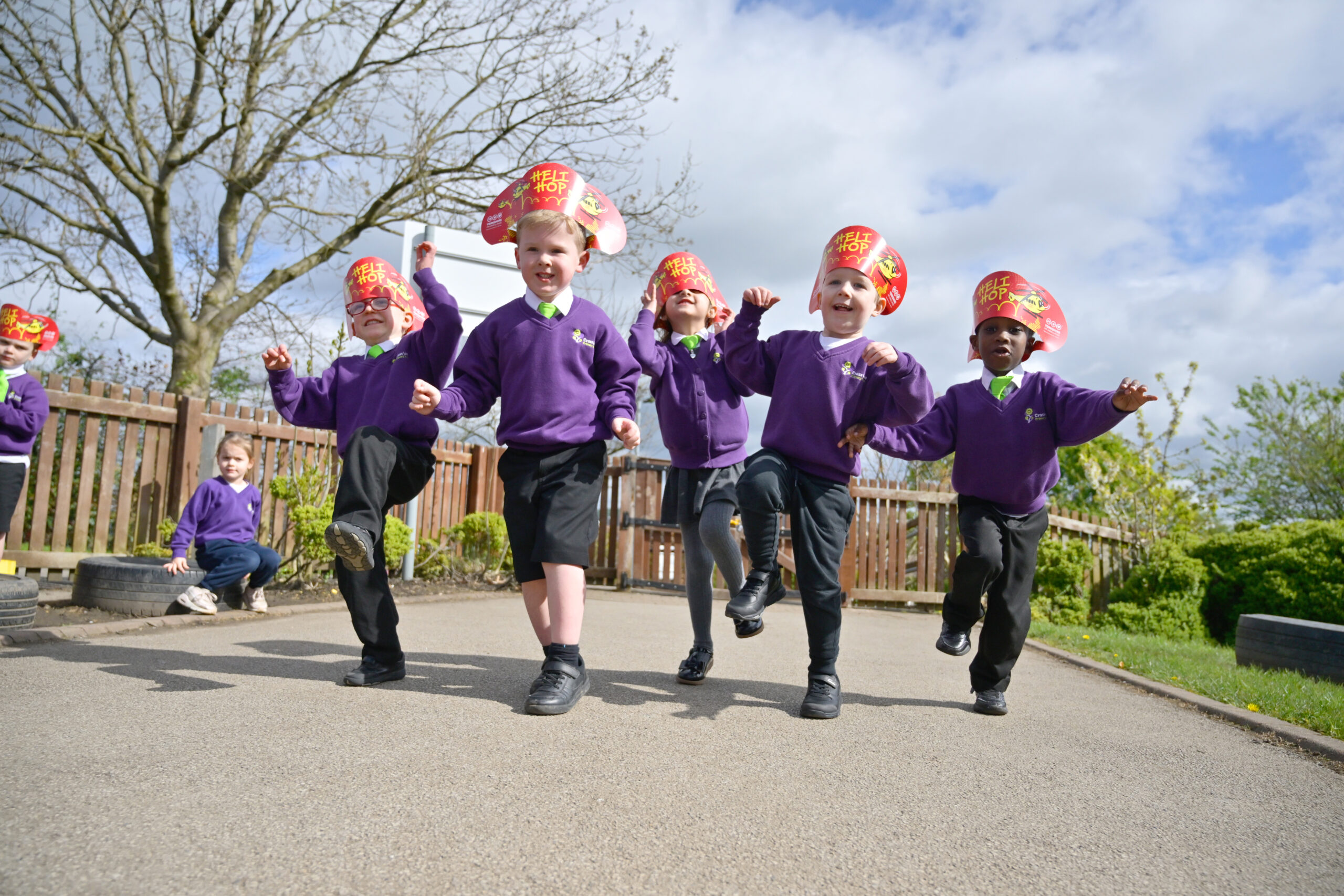 A group of children wearing purple sweatshirts and red and yellow headbands are hopping towards the camera.