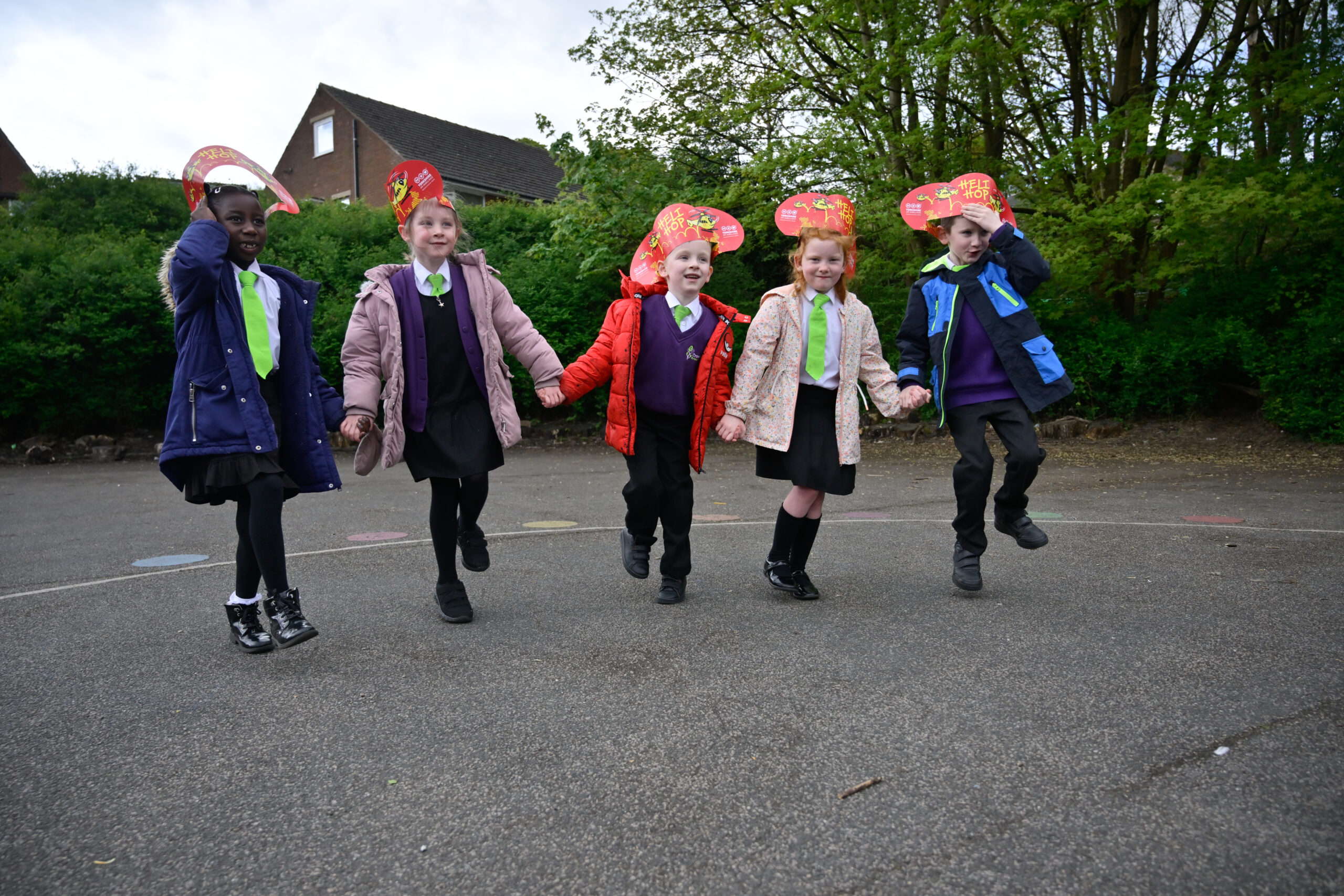 A group of children wearing red headbands that say 'HELI HOP' on them are holding hands and hopping