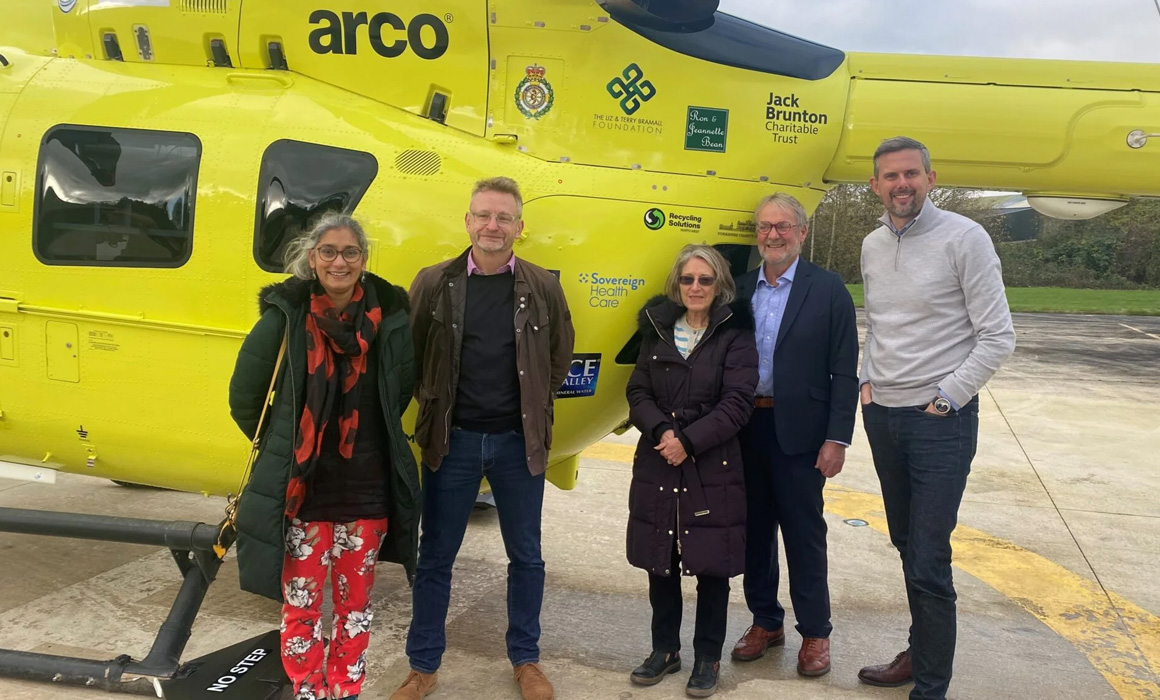 A group of people standing in front of a yellow helicopter.