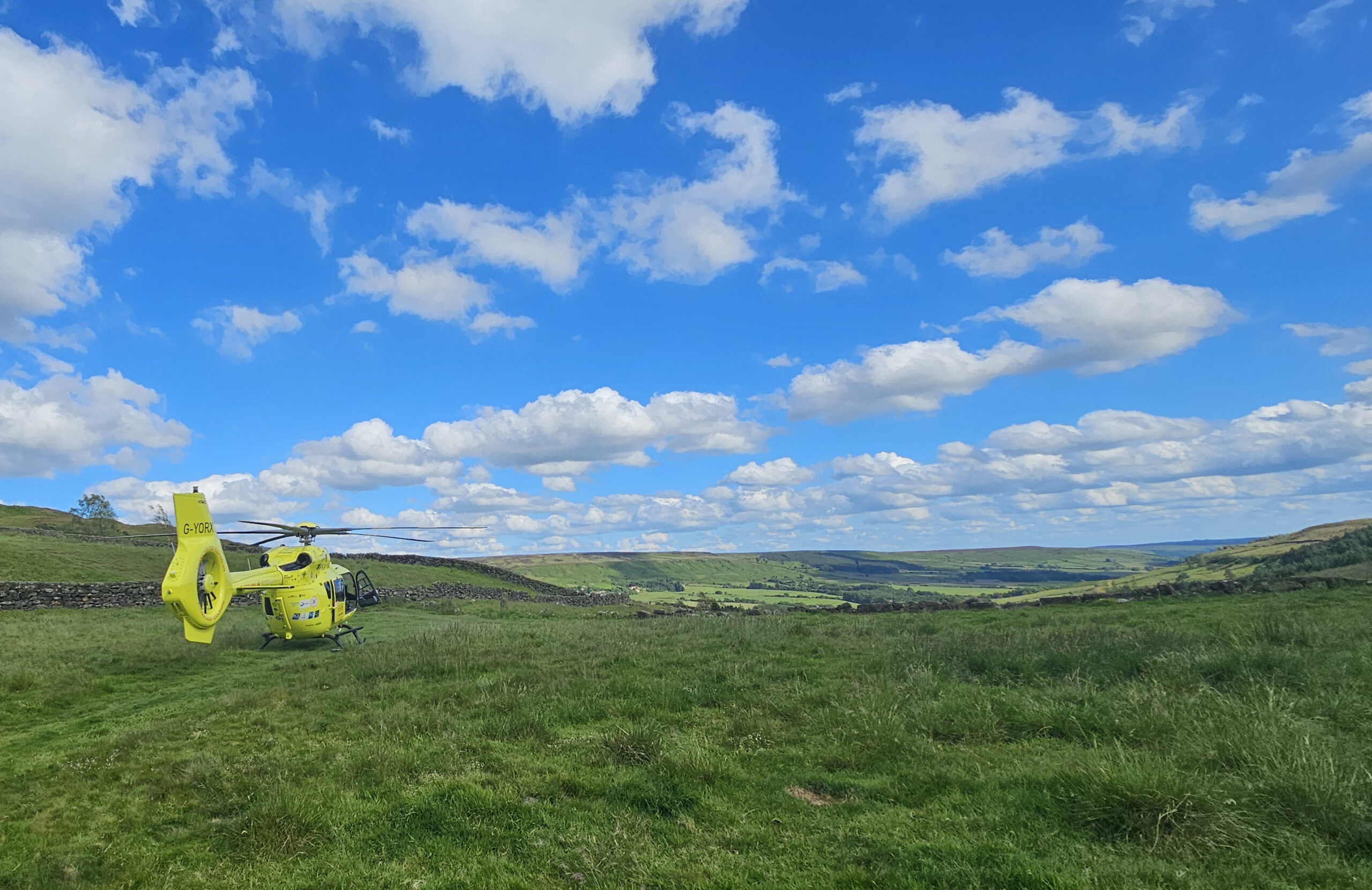 WILLS AND LEGACIES - YOUR LASTING LEGACY A yellow helicopter landed on a green field with a dry stone wall in the background