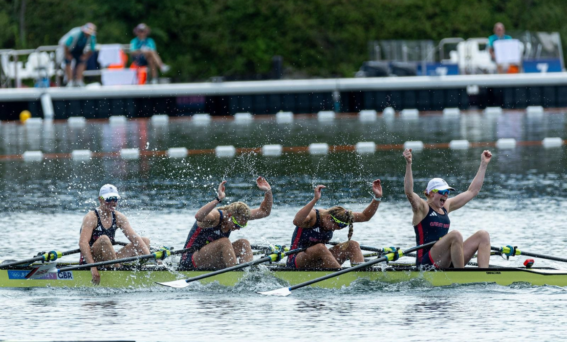 Four people in a rowing boat, lifting their arms in celebration