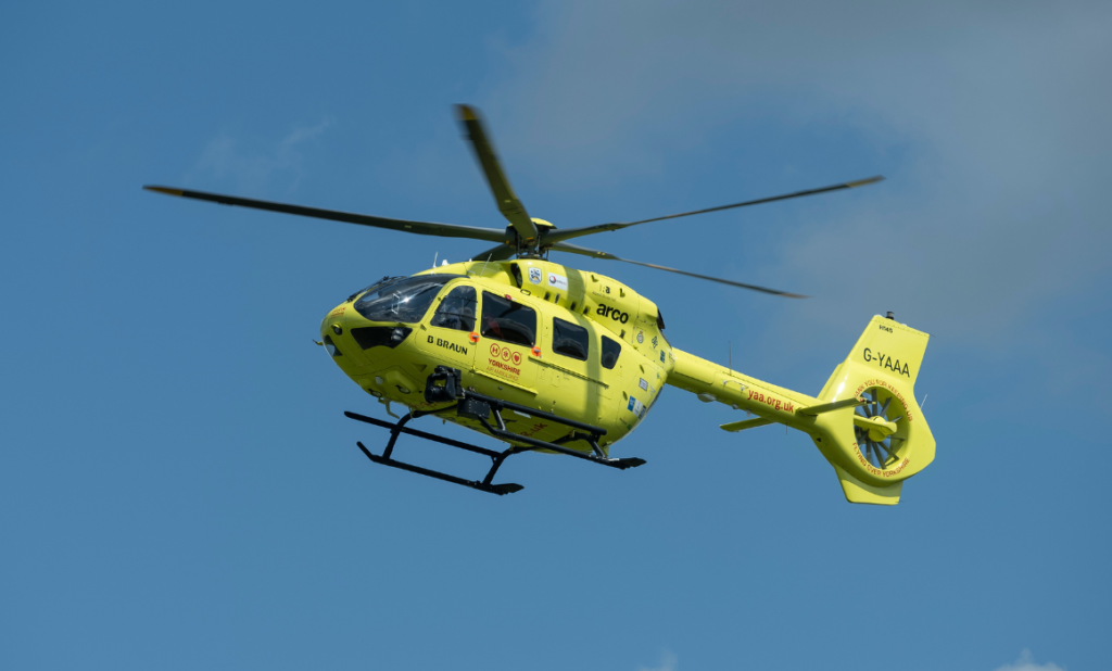 A yellow helicopter flying through a blue sky