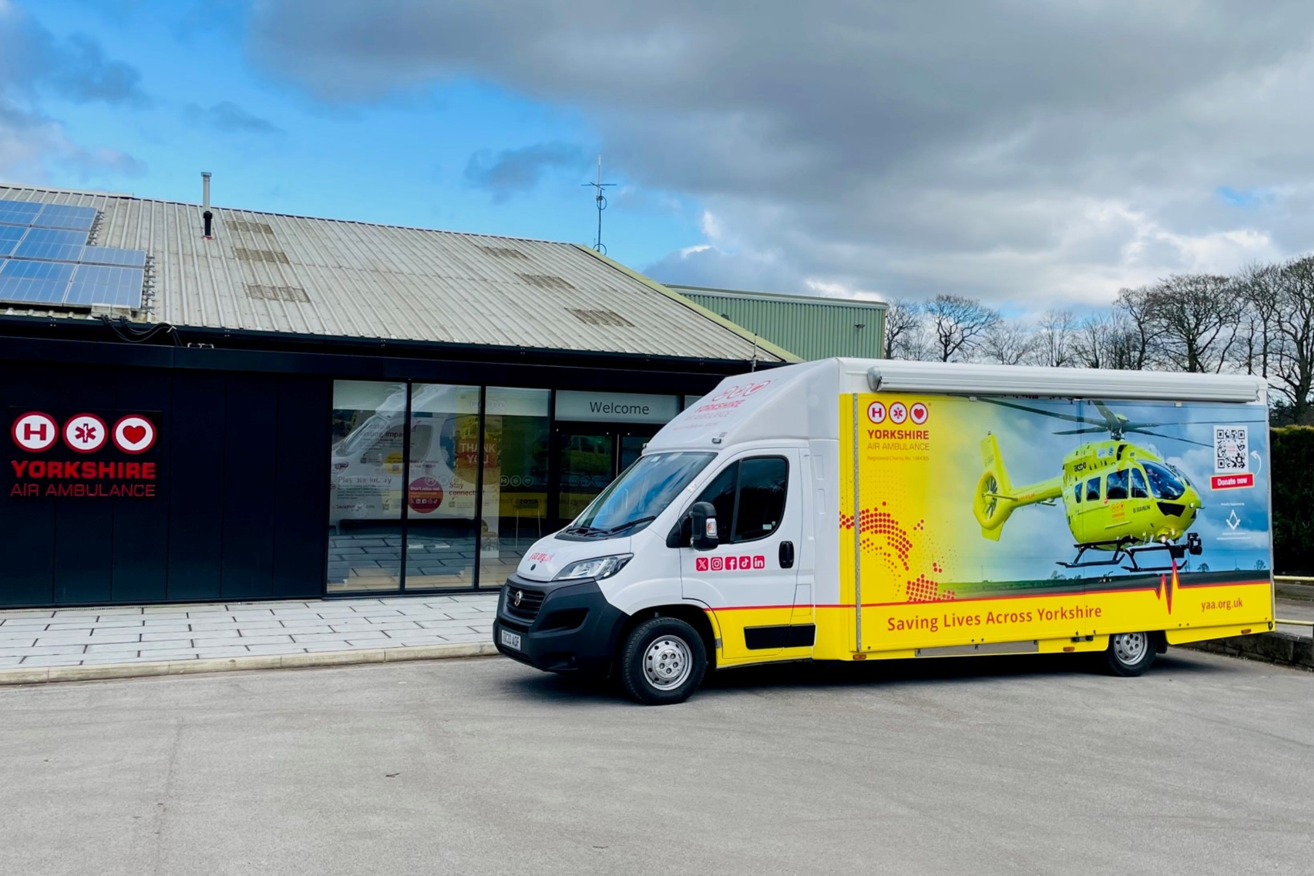 A van which bright graphics featuring a yellow helicopter is parked outside a building with a black front, featuring large windows and a red logo.