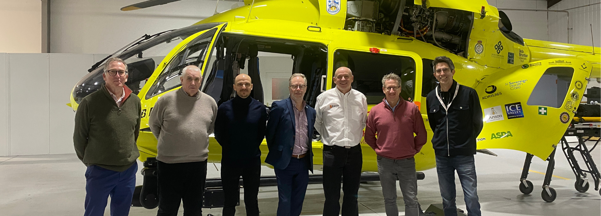 Seven men stood in front of a yellow helicopter