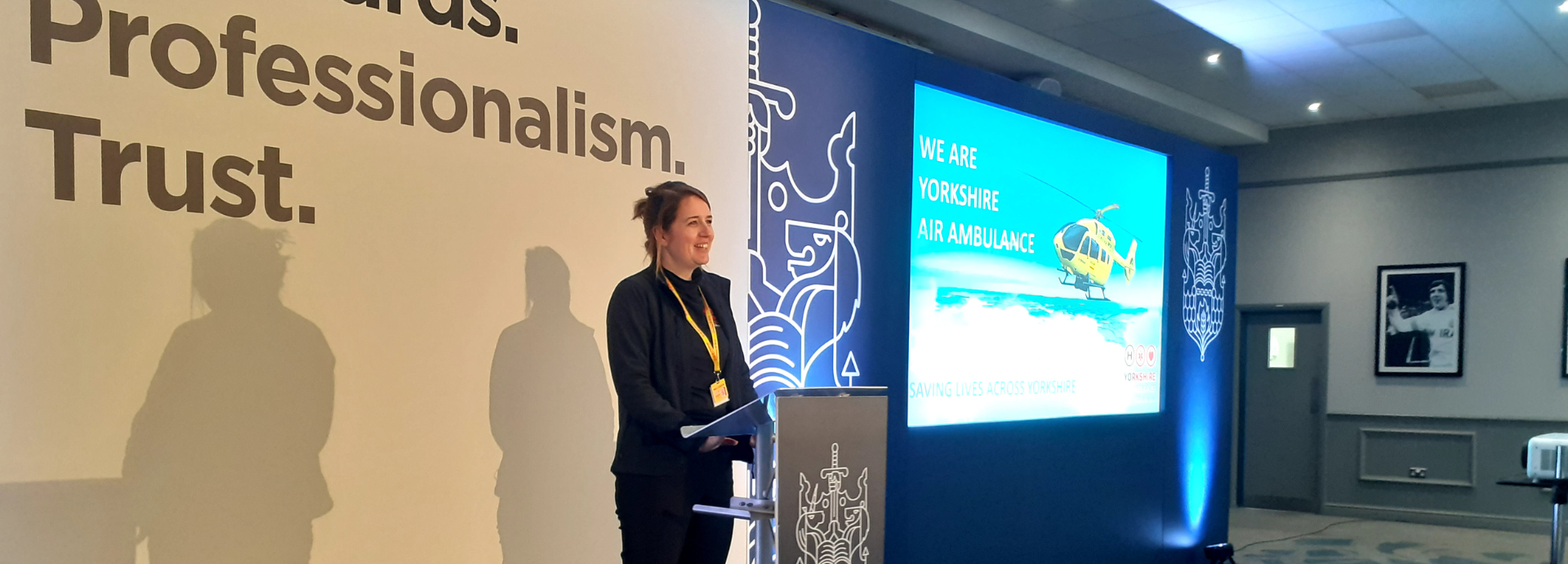 A lady is stood on a stage presenting in front of a big screen