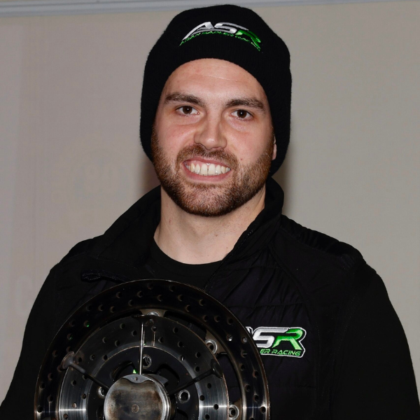 A man wearing a black beanie hat and a black fleece jacket both with the same white and green logo on them. The man has a dark beard.
