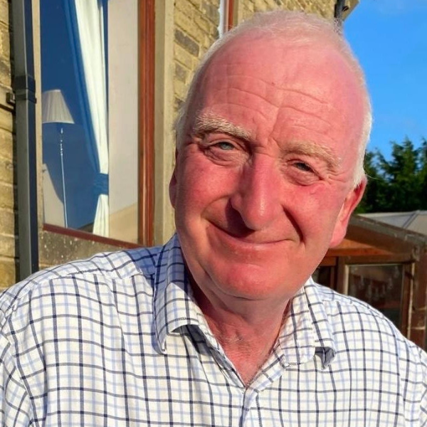 A man with white hair, wearing a light coloured checked shirt.