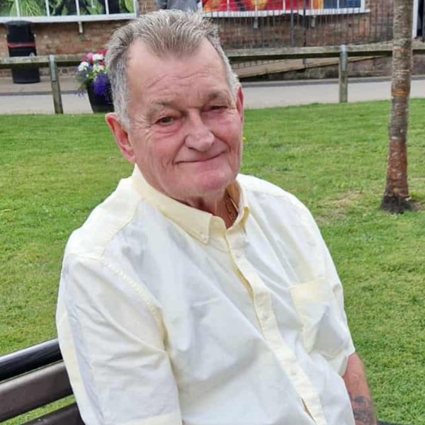 A man with grey hair wearing a light yellow short sleeved shirt.