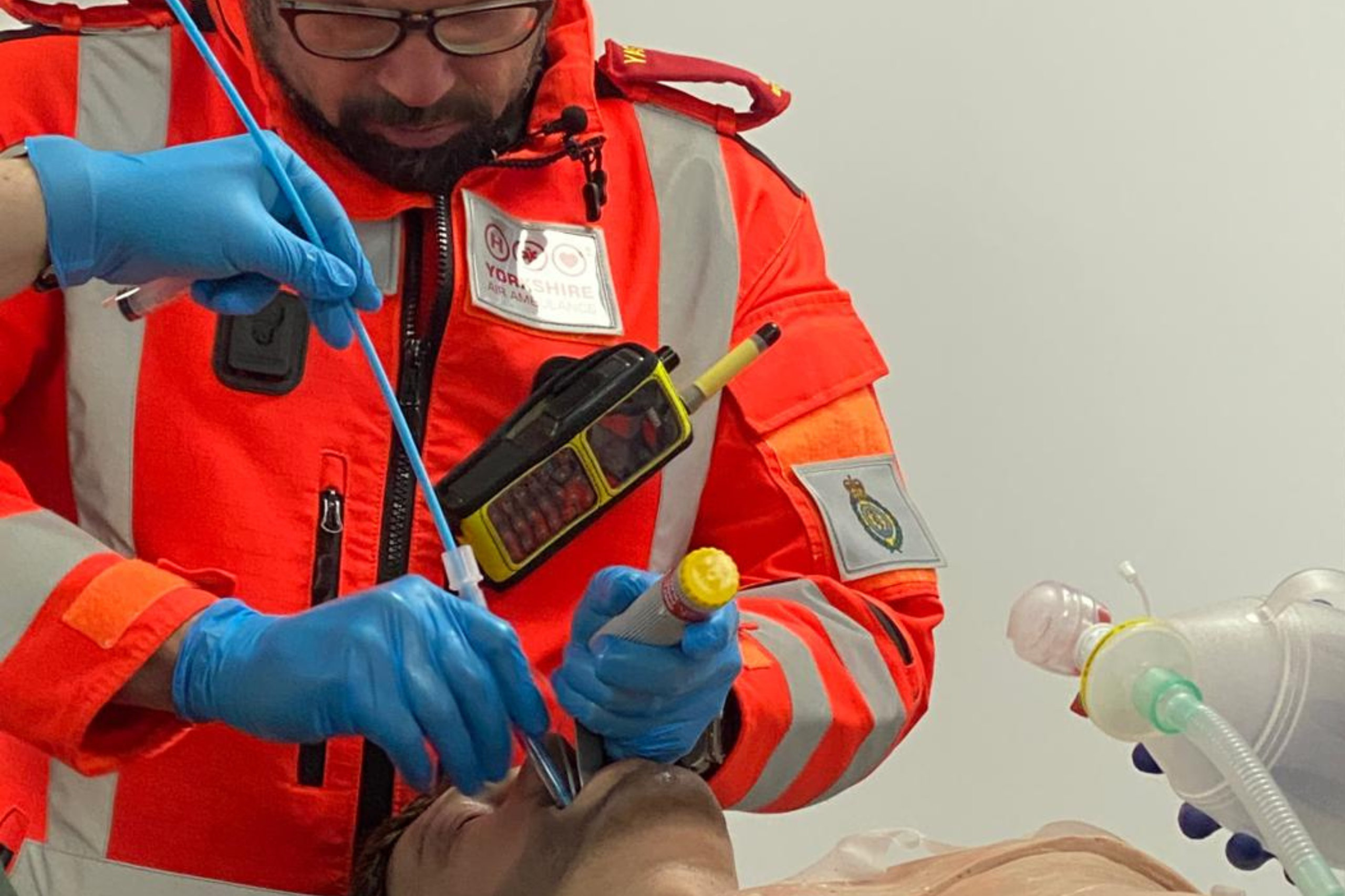 A doctor wearing an orange flight suit is carrying out a procedure on a model.